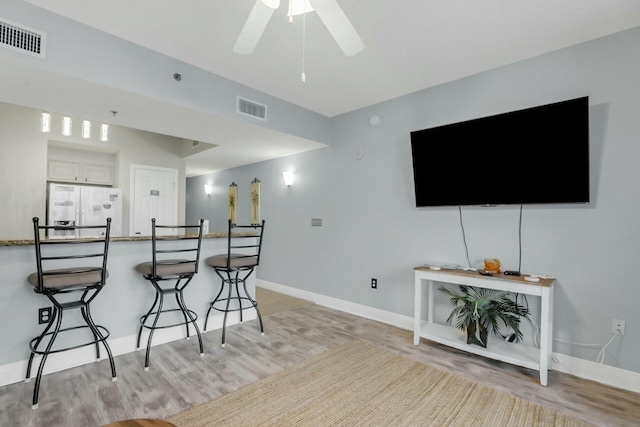 interior space featuring light wood-type flooring, a breakfast bar, ceiling fan, white refrigerator, and white cabinets