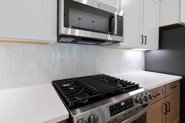 kitchen with stainless steel appliances, white cabinets, decorative backsplash, and light stone countertops