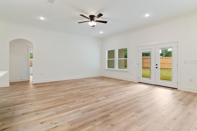 unfurnished living room featuring arched walkways, french doors, light wood-style floors, ornamental molding, and baseboards