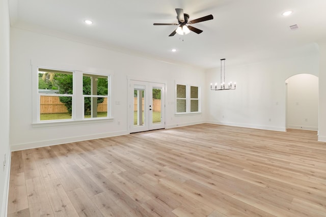 unfurnished living room with arched walkways, visible vents, ornamental molding, light wood-type flooring, and baseboards