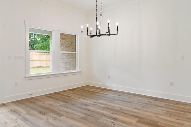 unfurnished room with a chandelier, crown molding, light wood-style flooring, and baseboards