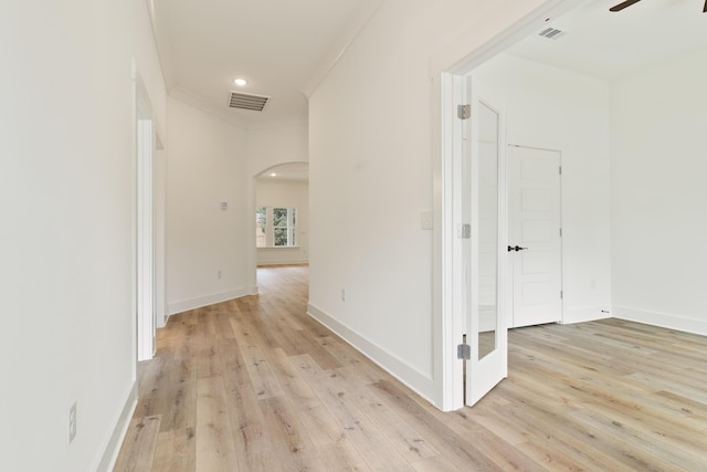 corridor featuring arched walkways, baseboards, visible vents, and light wood-style floors