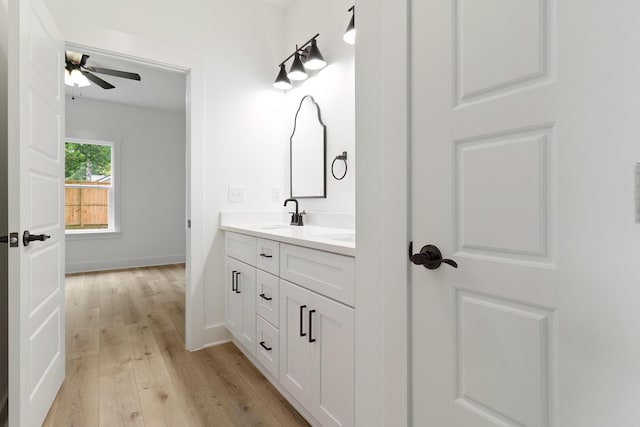 bathroom featuring double vanity, a ceiling fan, a sink, wood finished floors, and baseboards