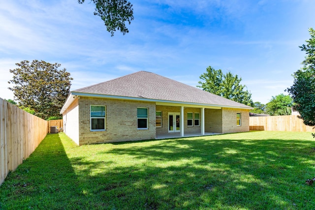 rear view of house featuring central AC unit, a fenced backyard, brick siding, french doors, and a lawn