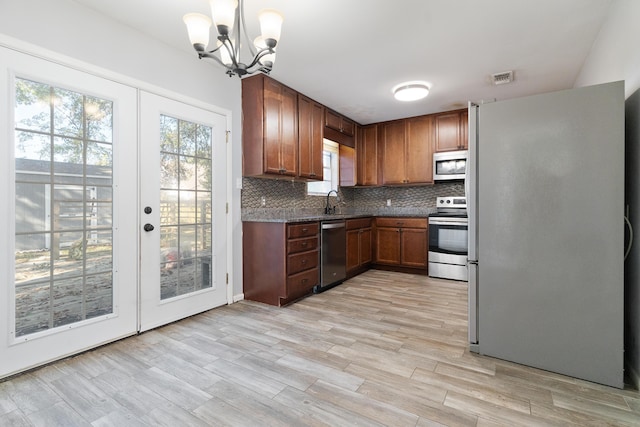 kitchen featuring stainless steel appliances, a chandelier, decorative light fixtures, light hardwood / wood-style floors, and decorative backsplash