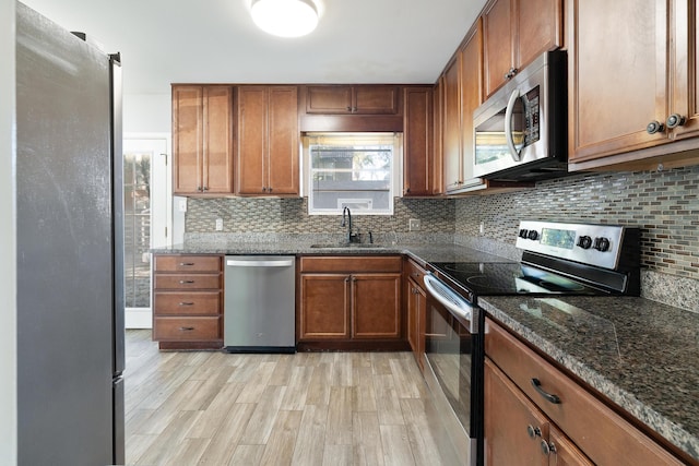 kitchen with backsplash, sink, light hardwood / wood-style flooring, dark stone countertops, and appliances with stainless steel finishes