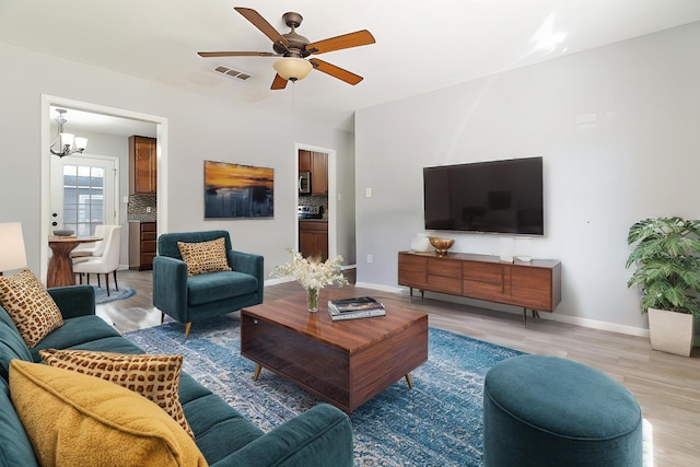 living room with ceiling fan with notable chandelier and light wood-type flooring