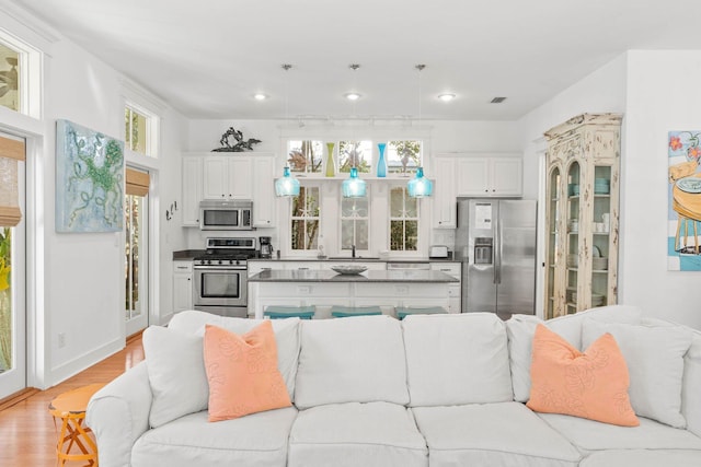 kitchen with decorative backsplash, appliances with stainless steel finishes, light hardwood / wood-style flooring, white cabinets, and hanging light fixtures