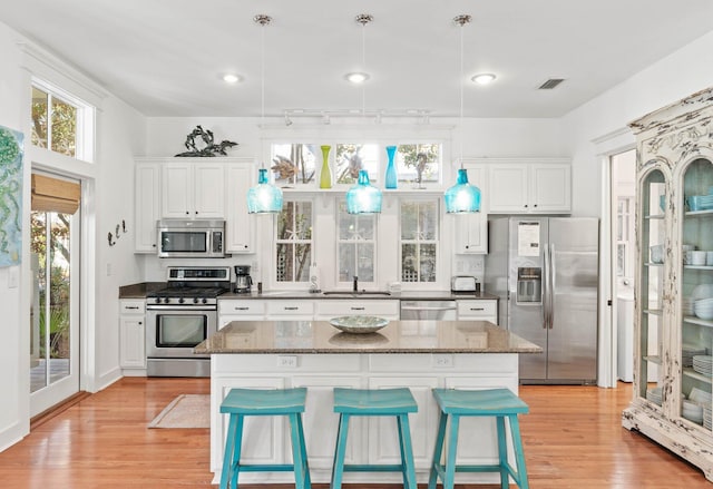 kitchen with a kitchen bar, white cabinetry, hanging light fixtures, and stainless steel appliances