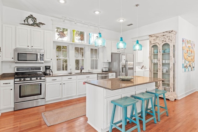 kitchen with a center island, washing machine and dryer, a breakfast bar, white cabinets, and appliances with stainless steel finishes