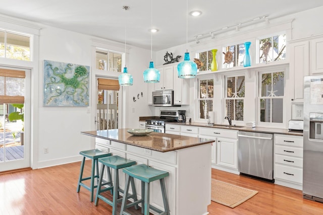 kitchen featuring appliances with stainless steel finishes, sink, decorative light fixtures, dark stone countertops, and white cabinetry