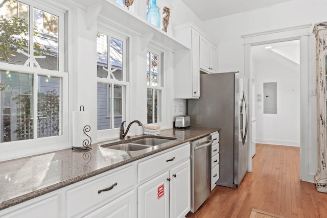 kitchen featuring light wood-type flooring, dark stone counters, stainless steel appliances, sink, and white cabinetry