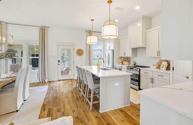 kitchen with sink, decorative light fixtures, a kitchen island with sink, white cabinets, and appliances with stainless steel finishes