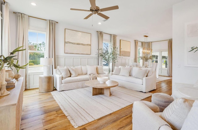 living room featuring ceiling fan with notable chandelier and light wood-type flooring