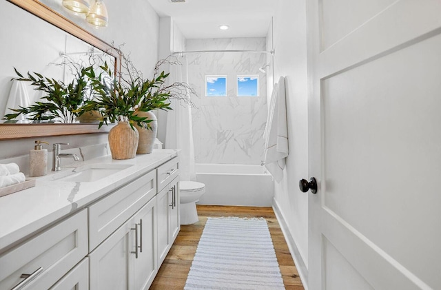 full bathroom with vanity, hardwood / wood-style floors, tiled shower / bath, and toilet