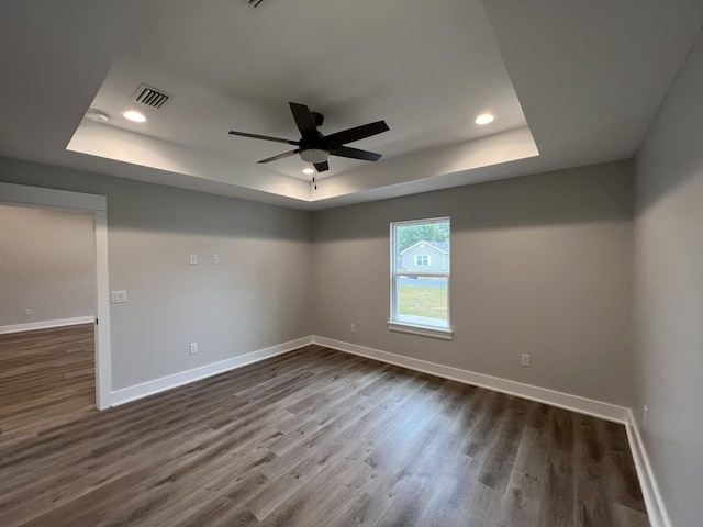 empty room featuring ceiling fan, a tray ceiling, and dark hardwood / wood-style floors