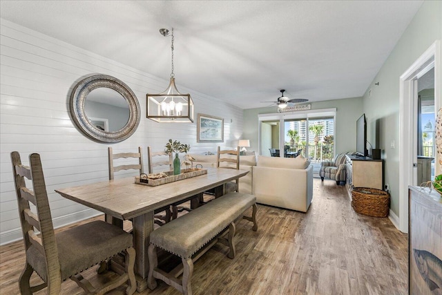 dining area featuring hardwood / wood-style floors, ceiling fan with notable chandelier, and wood walls