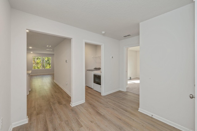 hallway with light hardwood / wood-style floors, washing machine and dryer, and a textured ceiling