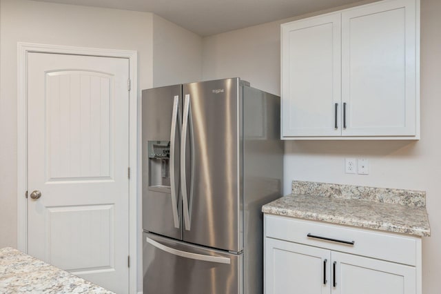 kitchen featuring stainless steel fridge, light stone countertops, and white cabinetry