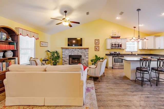 living room with vaulted ceiling, ceiling fan, sink, light hardwood / wood-style flooring, and a stone fireplace