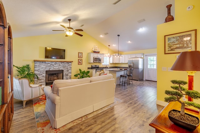 living room featuring ceiling fan, a fireplace, vaulted ceiling, and light hardwood / wood-style flooring