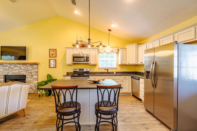 kitchen with hanging light fixtures, lofted ceiling, a kitchen bar, white cabinets, and appliances with stainless steel finishes