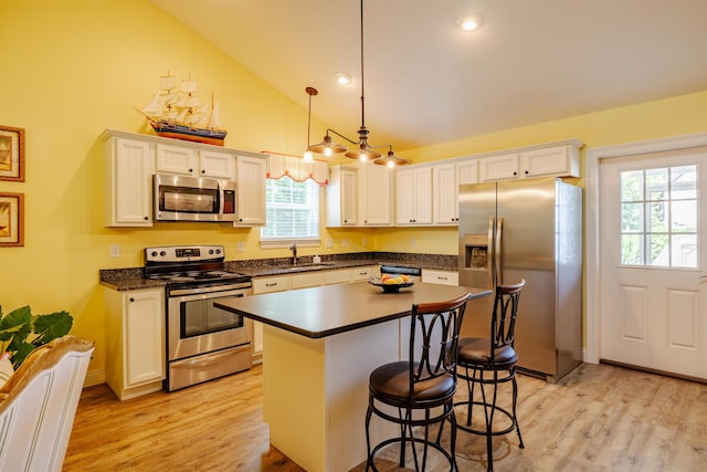 kitchen with stainless steel appliances, a kitchen island, sink, white cabinetry, and hanging light fixtures