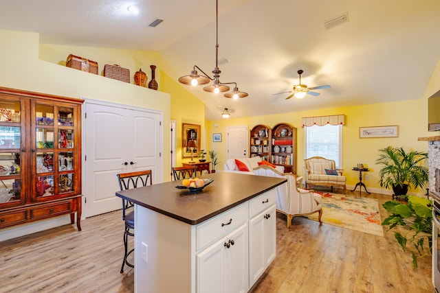 kitchen with a kitchen breakfast bar, ceiling fan, decorative light fixtures, light hardwood / wood-style flooring, and white cabinets