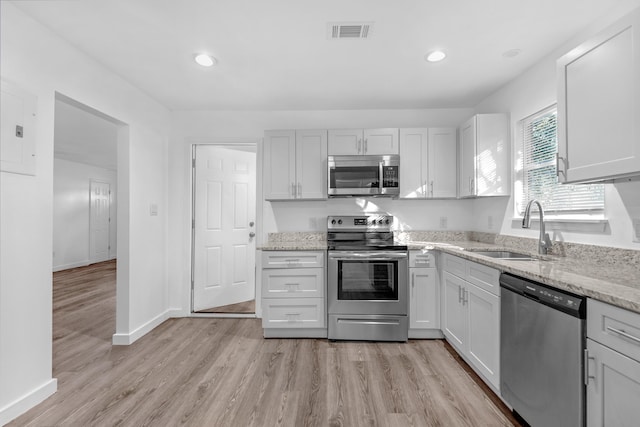 kitchen featuring light stone countertops, sink, stainless steel appliances, and light hardwood / wood-style flooring