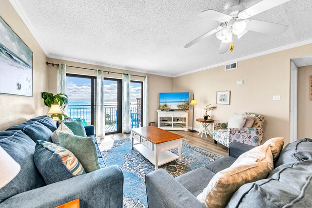 living room featuring a textured ceiling, hardwood / wood-style flooring, ceiling fan, and crown molding