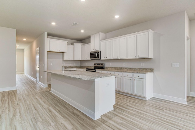 kitchen featuring white cabinetry, sink, stainless steel appliances, light stone counters, and a kitchen island with sink