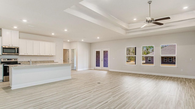 kitchen featuring white cabinets, light hardwood / wood-style flooring, light stone countertops, an island with sink, and stainless steel appliances