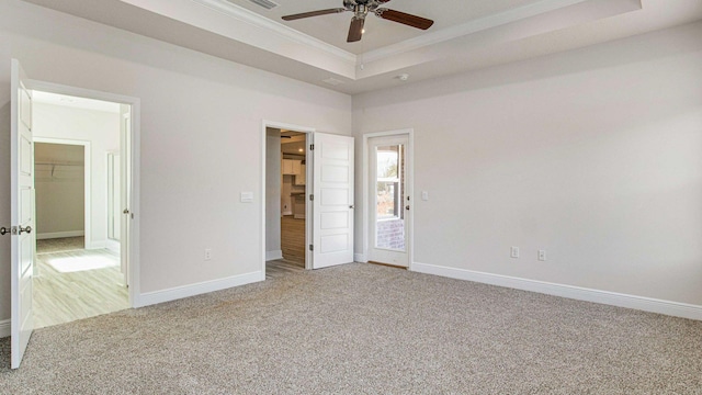 unfurnished bedroom featuring a walk in closet, a tray ceiling, ceiling fan, crown molding, and carpet floors