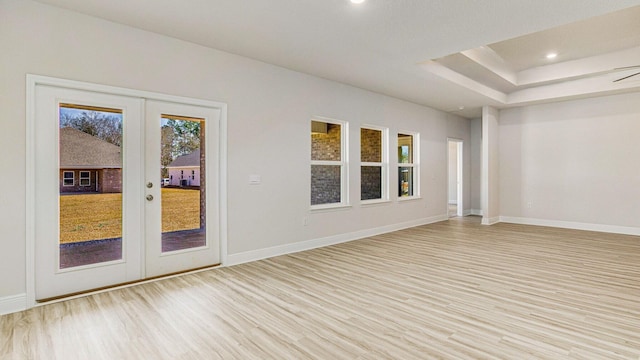 empty room featuring french doors, light wood-type flooring, a raised ceiling, and ceiling fan