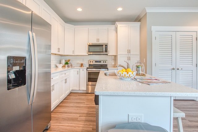 kitchen featuring decorative backsplash, white cabinets, an island with sink, and appliances with stainless steel finishes