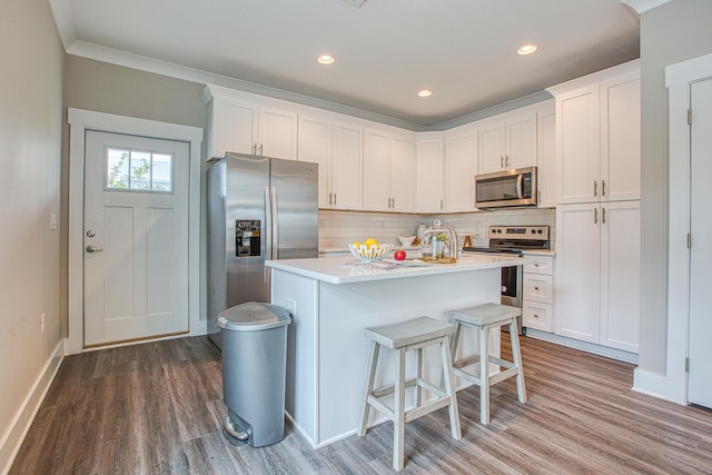 kitchen featuring tasteful backsplash, stainless steel appliances, a kitchen island, wood-type flooring, and white cabinetry