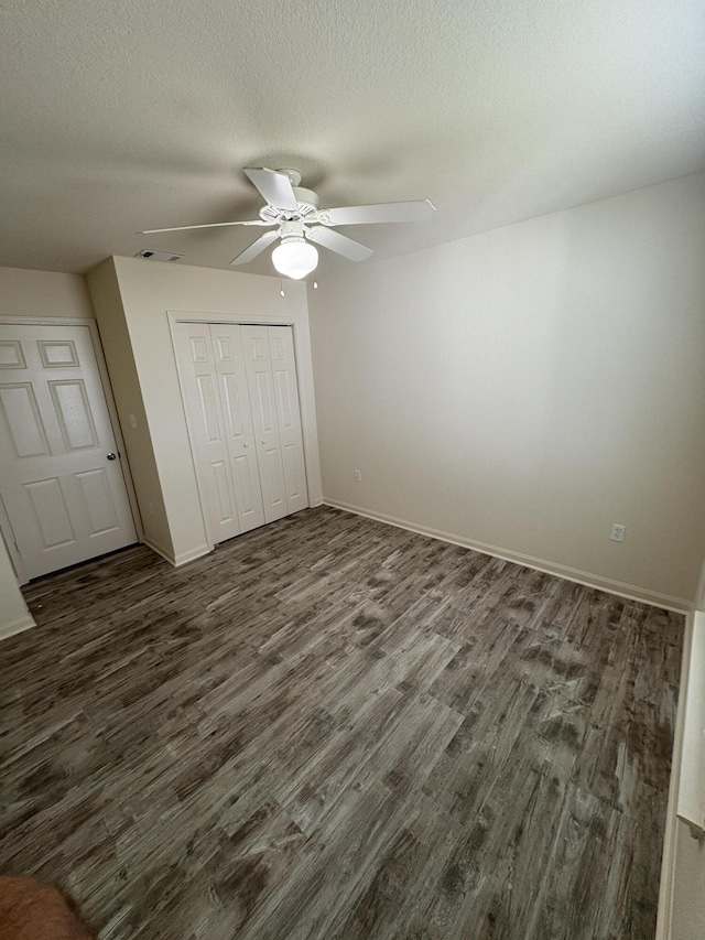 unfurnished bedroom featuring dark hardwood / wood-style flooring, ceiling fan, a closet, and a textured ceiling