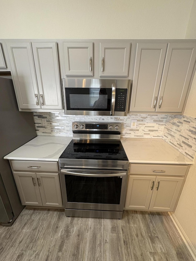 kitchen featuring light stone countertops, appliances with stainless steel finishes, decorative backsplash, and wood-type flooring