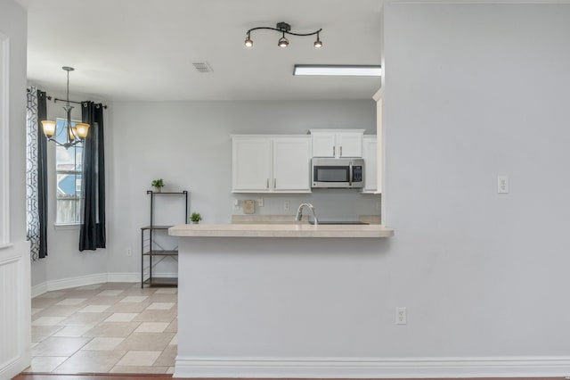 kitchen with white cabinetry, hanging light fixtures, an inviting chandelier, kitchen peninsula, and light tile patterned flooring