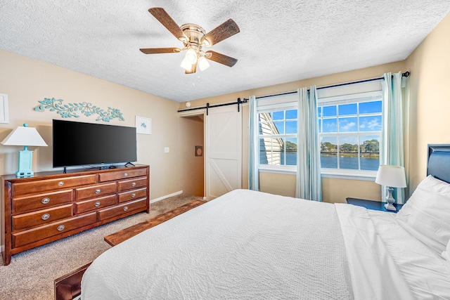 carpeted bedroom with ceiling fan, a barn door, a water view, and a textured ceiling