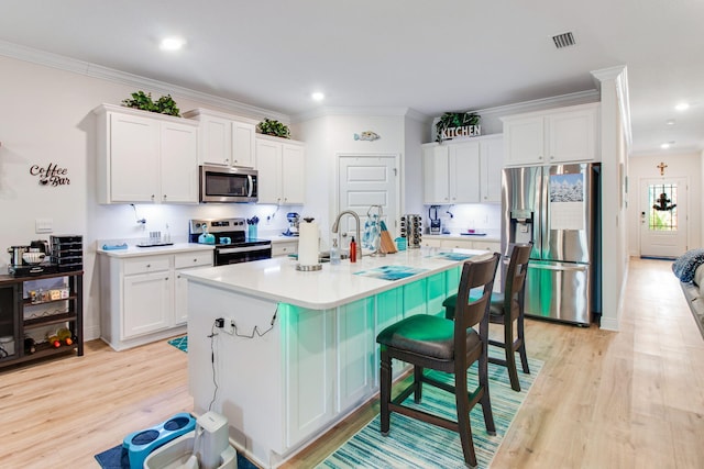 kitchen with white cabinets, a kitchen breakfast bar, appliances with stainless steel finishes, and light hardwood / wood-style flooring