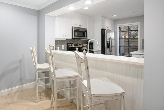 kitchen featuring appliances with stainless steel finishes, backsplash, a kitchen breakfast bar, white cabinetry, and light tile patterned flooring