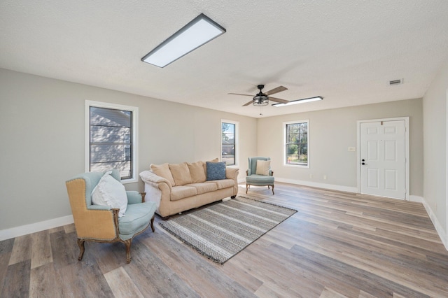 living room with ceiling fan, a textured ceiling, and light wood-type flooring