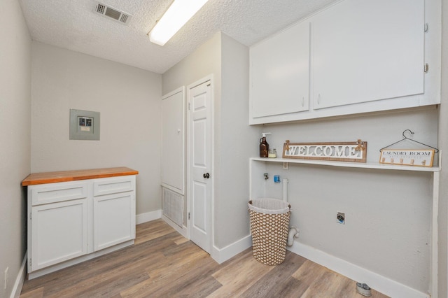 laundry area with electric dryer hookup, light hardwood / wood-style floors, cabinets, and a textured ceiling