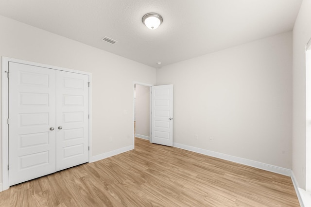 unfurnished bedroom featuring a textured ceiling, light hardwood / wood-style floors, and a closet