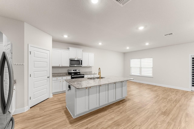 kitchen with appliances with stainless steel finishes, light stone counters, a kitchen island with sink, sink, and white cabinets