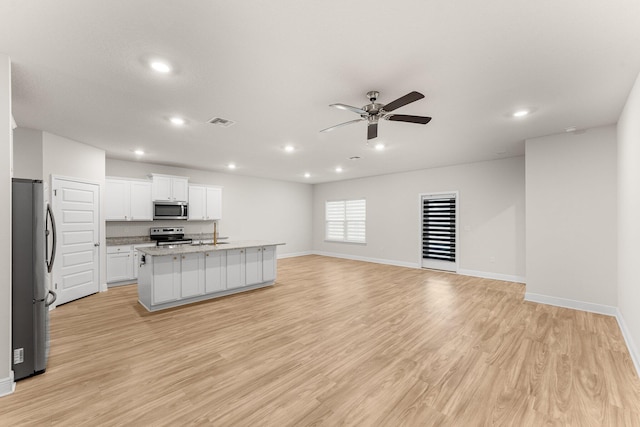 kitchen featuring appliances with stainless steel finishes, light stone counters, light hardwood / wood-style floors, white cabinetry, and an island with sink