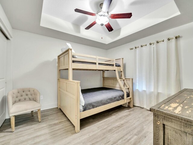 bedroom with a tray ceiling, ceiling fan, and light hardwood / wood-style flooring