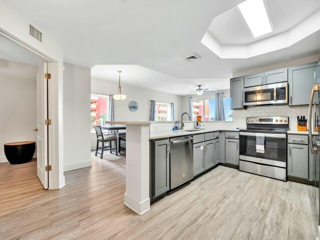 kitchen with ceiling fan, sink, light hardwood / wood-style flooring, kitchen peninsula, and appliances with stainless steel finishes