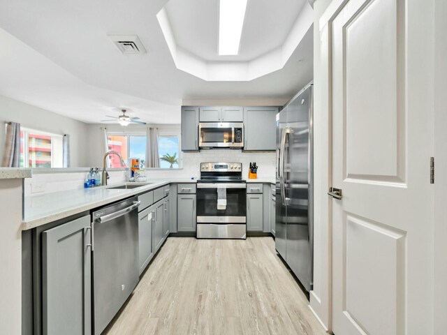 kitchen featuring gray cabinetry, sink, ceiling fan, a tray ceiling, and stainless steel appliances